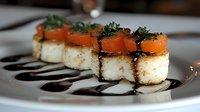 Pan-seared scallops topped with fresh tomato slices and micro herbs, drizzled with balsamic reduction on white plate, elegant restaurant presentation.