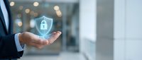 Businessman in dark suit holding glowing digital security shield with padlock icon, representing data protection and cybersecurity solutions for enterprise networks.