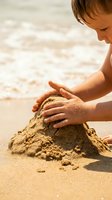 Young boy building sandcastle on sunny beach with golden sand and ocean waves in background during summer vacation.
