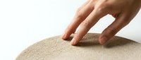 Hand touching soft beige textured surface with gentle finger contact on neutral background for sensory design concepts.