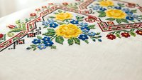 Traditional Ukrainian embroidery with colorful floral patterns on white linen fabric featuring yellow roses and blue flowers in cross-stitch technique.