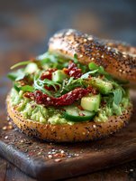 Fresh avocado toast on seeded bagel with arugula, sun-dried tomatoes and cucumber for healthy breakfast or lunch meal preparation.