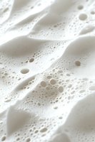 White soap foam texture with bubbles and soft waves creating abstract pattern. Macro photography showing delicate details of cleaning product lather.