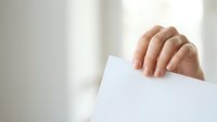 Close-up of hand holding blank white paper against light background, suitable for business communications, announcements, and marketing materials.