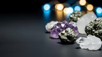 Collection of healing crystals and gemstones including amethyst, pyrite, and clear quartz arranged on dark surface with bokeh lights for meditation and wellness.