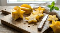 Fresh star fruit slices on rustic wooden cutting board with knife and mint garnish for healthy tropical cooking and food preparation.