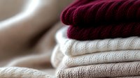 Neatly folded stack of cozy knitted sweaters in burgundy and neutral beige tones, showcasing different textures and patterns in warm winter clothing.