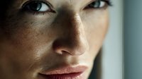 Close up portrait of young Caucasian woman with freckles and natural makeup in soft window light showing confidence and natural beauty.