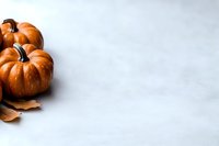 Orange pumpkins with autumn leaves on white marble background with copy space for fall seasonal design and harvest celebration projects.
