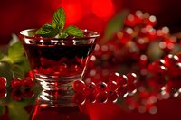 Fresh red currant dessert in glass with mint garnish against vibrant bokeh background of berries, creating festive holiday atmosphere.