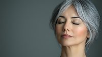 Serene mature Asian woman with silver gray hair and closed eyes against dark background showing peaceful expression and natural aging gracefully.