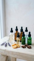 Natural essential oil bottles with dropper caps arranged on wooden surface with dried lavender, orange slices and star anise for aromatherapy and wellness.