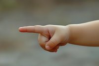 Small child's hand pointing finger against blurred natural background, showing direction or making choice with innocent gesture. Soft focus creates gentle mood.