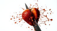 Fresh red strawberry being sliced with sharp knife creating dynamic splash of juice and fruit pieces on clean white background for culinary designs.