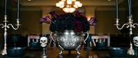 Ornate silver urn with dark purple flowers flanked by candelabras and skulls creates dramatic gothic centerpiece for Halloween or horror themed events.