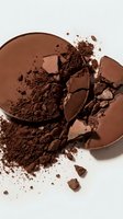 Crushed and broken chocolate powder compacts with loose cocoa dust scattered on white surface, showcasing makeup or cosmetic product texture and application.
