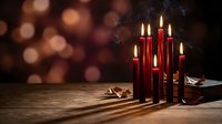 Red candles burning on wooden table with warm bokeh lights creating cozy atmospheric holiday ambiance for seasonal celebrations and festive decorations.