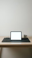 Laptop with blank screen on dark felt desk pad, styled workspace setup with ceramic mug and office supplies on wooden table for remote work and business mockups.