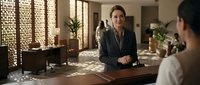 Professional businesswoman in dark suit conducting meeting in modern office with decorative screens and natural lighting for corporate presentations.