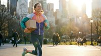 Young athletic woman jogging in urban park during golden hour sunrise, wearing colorful sportswear and headphones for healthy lifestyle and fitness.