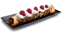 Crispy cannoli filled with sweet ricotta cream, topped with fresh raspberries and drizzled with dark chocolate sauce, served on black rectangular plate.