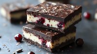 Layered chocolate cranberry cheesecake bars with dark chocolate ganache topping and fresh berries on rustic background, macro food photography for dessert menu.