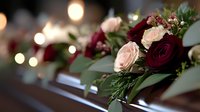 Romantic floral arrangement with burgundy and blush roses adorned with greenery on wooden surface against soft bokeh lights background for wedding decor.