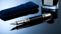 Luxury fountain pen with chrome and black finish displayed on reflective surface alongside blue velvet case and ink bottle for writing, calligraphy, and professional correspondence.