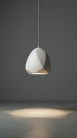 Modern white pendant lamp with geometric faceted design hanging from cord, casting warm light on concrete floor, suitable for interior design, home decor, and lighting concepts.
