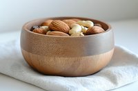 Mixed nuts including almonds, walnuts, and cashews in wooden bowl on white linen cloth for healthy snacking and cooking ingredients.