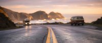 Vehicles traveling on coastal highway at sunset with mountains and ocean in background, suitable for travel, transportation, and adventure themed projects.