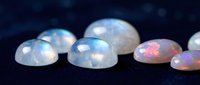 Collection of polished opal gemstones displaying iridescent fire and rainbow colors on dark surface for jewelry making and luxury accessories.