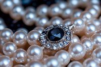 Elegant vintage style ring with dark blue sapphire gemstone and diamond accents resting on lustrous pearl necklace strand against soft blurred background.