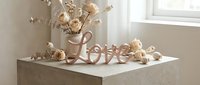Elegant rose gold Love sign with dried flowers and roses on a concrete pedestal, soft neutral tones, romantic home decor styling.
