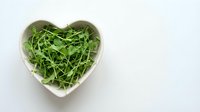 Fresh green arugula leaves in heart-shaped white bowl on clean background for healthy eating and nutrition concepts.