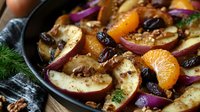 Fresh autumn salad with red apples, mandarin segments, cranberries and walnuts in cast iron pan garnished with herbs and spices for seasonal menu.
