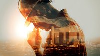 Double exposure of American flag and city skyline with silhouette figure at sunset, symbolizing patriotism and urban American identity.