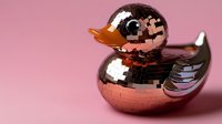 Metallic rose gold rubber duck sculpture with reflective mosaic disco ball surface pattern on pink background. Decorative modern art piece for contemporary decor.