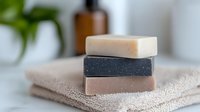 Natural handmade soap bars stacked on beige towel with blurred bathroom setting background, organic skincare and zero waste concept for sustainable living.