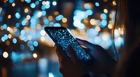 Silhouetted hands holding smartphone with glowing screen against blurred bokeh lights background creating magical evening atmosphere and digital connection concept.