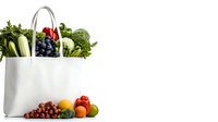 Fresh produce and groceries in white shopping bag with fruits and vegetables spilling out, healthy food shopping concept on white background.