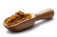 Ground turmeric powder in wooden scoop isolated on white background. Traditional Indian spice with bright orange color used in cooking and natural medicine.