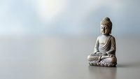 Serene Buddha statue in meditation pose on reflective surface with soft cloudy sky background for mindfulness and spiritual wellness concepts.