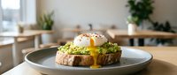 Poached egg with runny yolk on avocado toast served on a gray plate in a bright modern cafe interior.