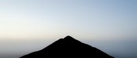 Silhouette of a mountain peak against a soft dawn or dusk sky with gradient colors transitioning from blue to pale orange, suitable for backgrounds and nature themes.