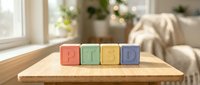 Colorful wooden blocks spelling PLDD arranged on natural wood table in bright living room with plants and window light, suitable for education and child development concepts.