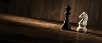 Chess pieces black king and white knight on wooden board with dramatic lighting creating strategic business concept for competition and planning.