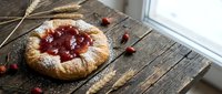 Rustic homemade cherry galette with golden pastry crust dusted with powdered sugar on wooden table with wheat stalks and fresh berries for bakery dessert.