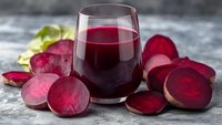 Fresh beetroot juice in glass with sliced beets on stone background, healthy detox drink rich in antioxidants and nutrients.