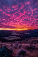 Dramatic purple and pink sunset sky over rolling hills and valleys with vibrant clouds creating stunning natural landscape scenery for backgrounds and travel content.